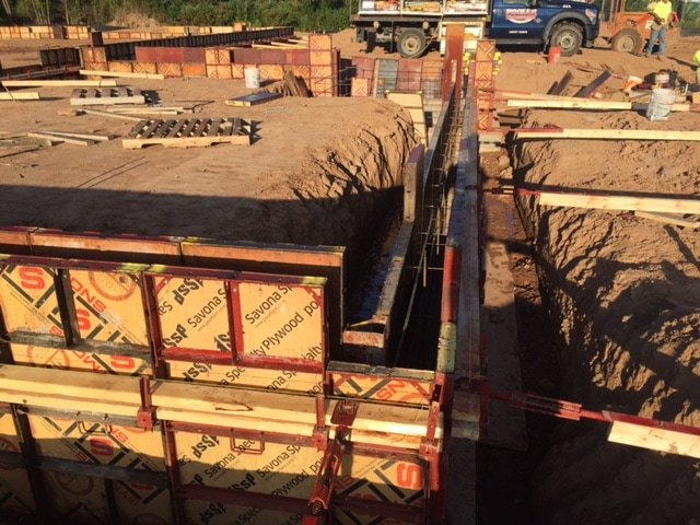Concrete formwork panels and red waler frames set into a foundation trench at sunset